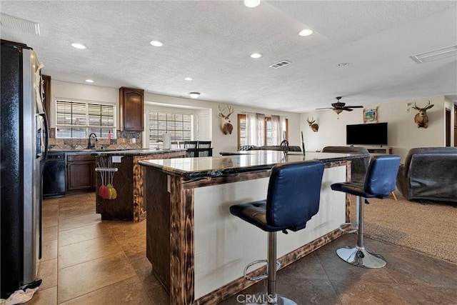 kitchen with dark countertops, a center island, open floor plan, a breakfast bar area, and freestanding refrigerator