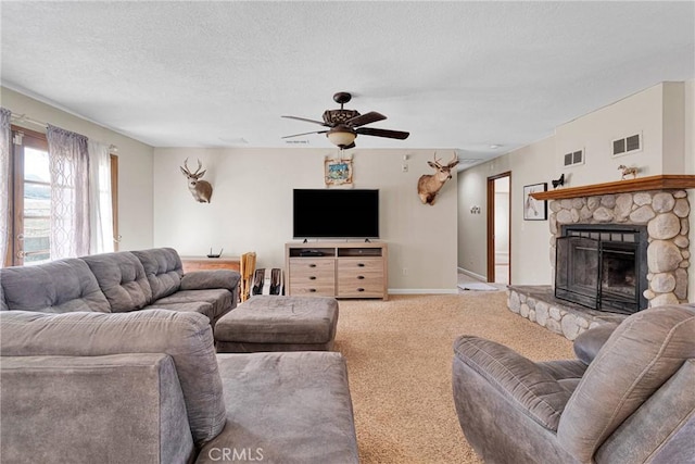 living area with a stone fireplace, carpet, visible vents, and a textured ceiling