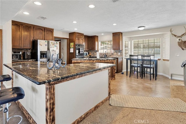 kitchen with visible vents, backsplash, black oven, stainless steel fridge with ice dispenser, and a kitchen bar