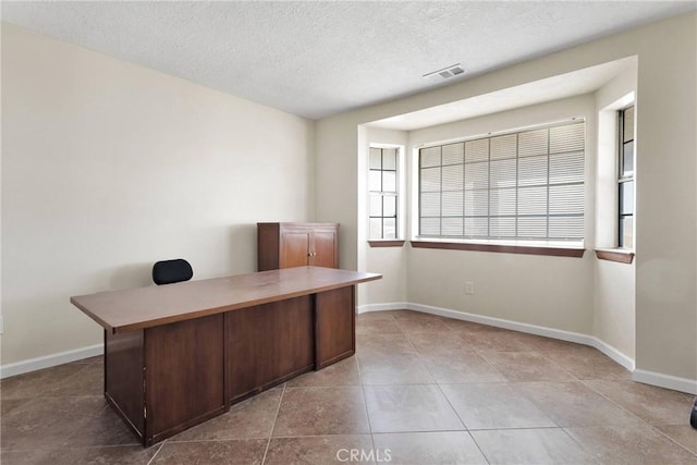 unfurnished office with light tile patterned floors, baseboards, visible vents, and a textured ceiling