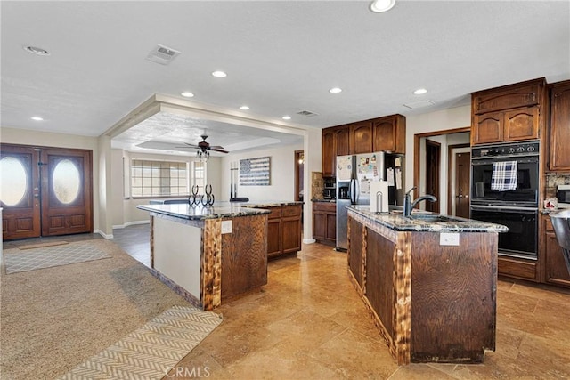 kitchen with dark stone countertops, visible vents, a center island with sink, and dobule oven black