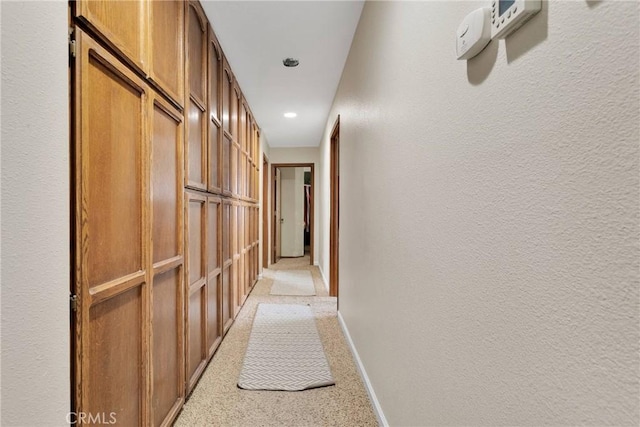 corridor with recessed lighting, baseboards, light carpet, and a textured wall