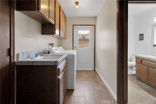 clothes washing area featuring baseboards, light tile patterned floors, separate washer and dryer, cabinet space, and a sink