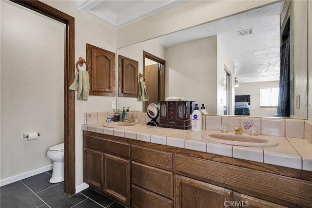 ensuite bathroom with double vanity, a sink, tile patterned flooring, ensuite bathroom, and toilet