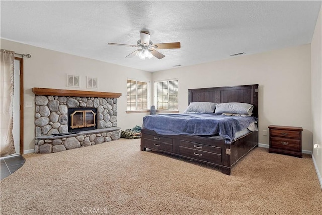 bedroom featuring visible vents, a textured ceiling, a stone fireplace, and carpet