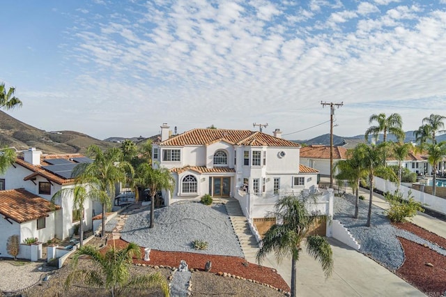 mediterranean / spanish-style house with stucco siding, fence, concrete driveway, a chimney, and a tiled roof