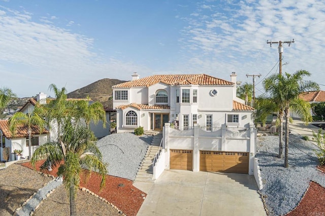 mediterranean / spanish-style house featuring stairway, a tiled roof, stucco siding, a chimney, and driveway