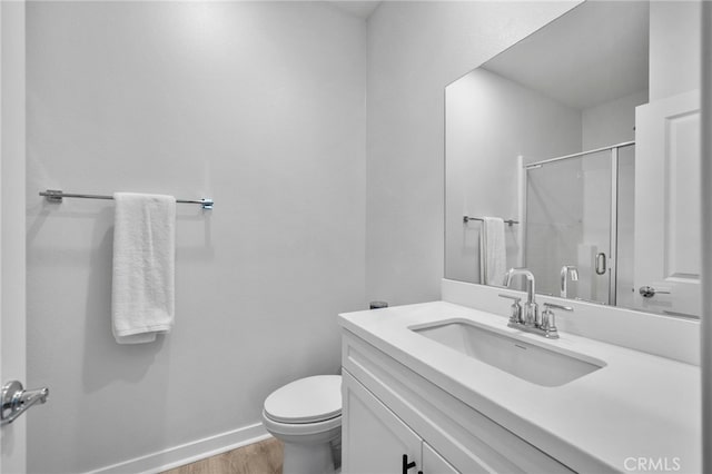 bathroom featuring vanity, wood finished floors, baseboards, toilet, and a shower with door