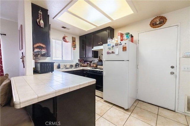 kitchen with visible vents, under cabinet range hood, tile countertops, a peninsula, and black appliances