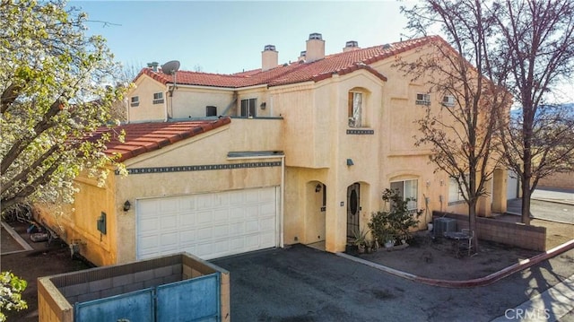 mediterranean / spanish-style house featuring stucco siding, driveway, a chimney, and a tiled roof