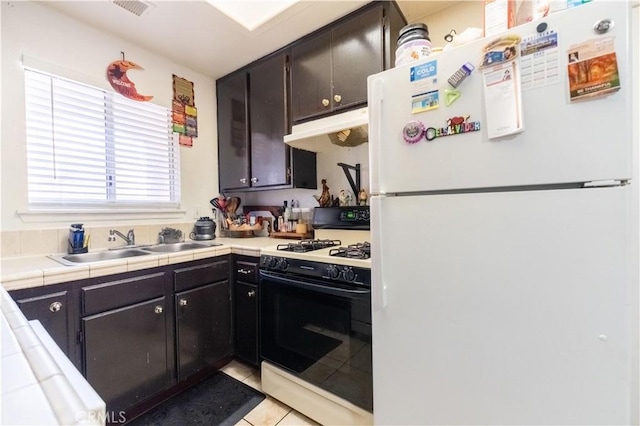 kitchen with under cabinet range hood, freestanding refrigerator, range with gas cooktop, light tile patterned floors, and tile counters