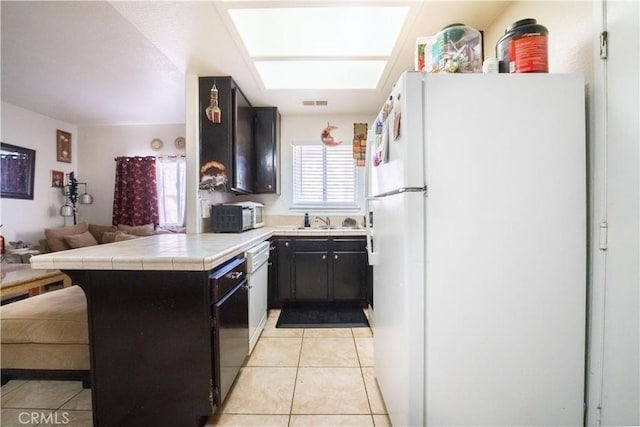 kitchen featuring open floor plan, light tile patterned floors, a peninsula, white appliances, and a sink