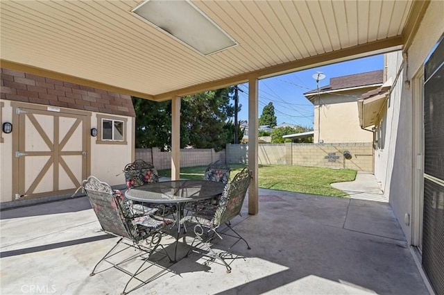 view of patio / terrace with a fenced backyard, an outbuilding, outdoor dining space, and a storage shed