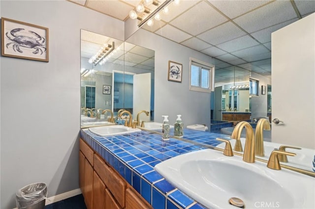 bathroom with a sink, a drop ceiling, and baseboards