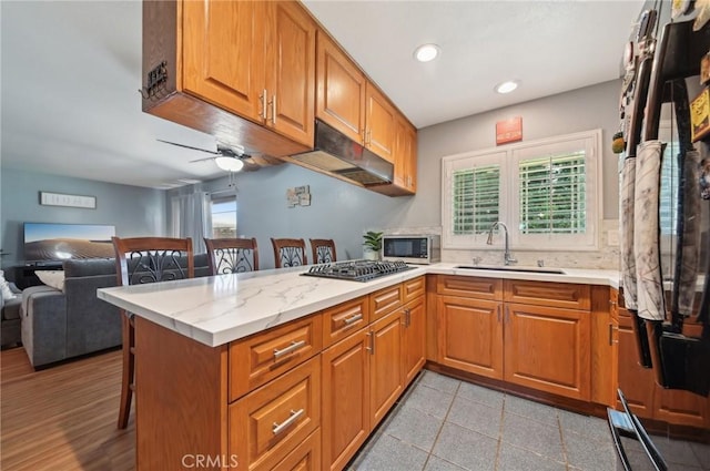 kitchen with a breakfast bar, a peninsula, stainless steel appliances, a sink, and brown cabinets