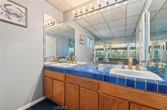 bathroom with double vanity, a drop ceiling, baseboards, and a sink