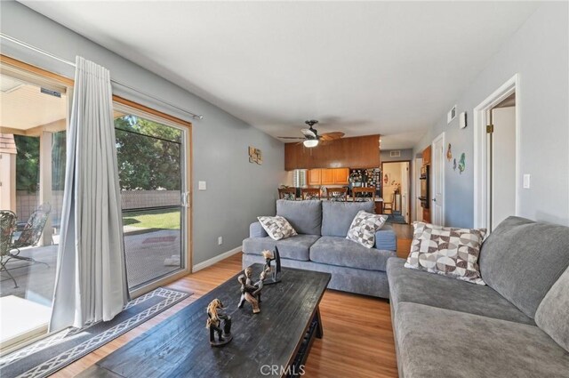 living area with light wood-style flooring, a ceiling fan, and baseboards