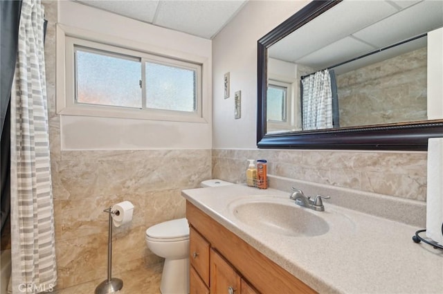 bathroom with toilet, curtained shower, tile walls, a paneled ceiling, and vanity