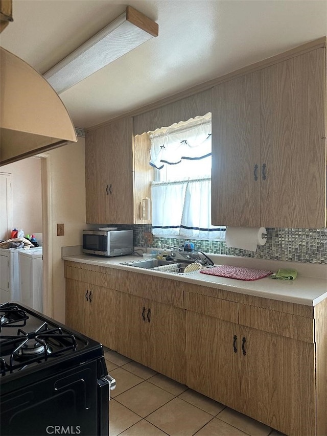 kitchen featuring washer and clothes dryer, stainless steel microwave, light countertops, light tile patterned floors, and black range with gas stovetop