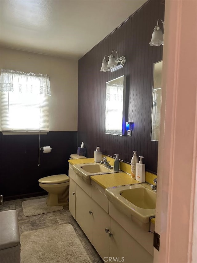 bathroom with double vanity, wood walls, toilet, and a sink