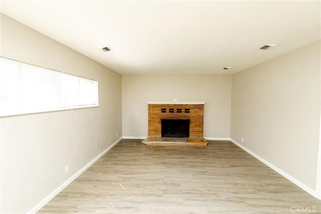 unfurnished living room with visible vents, a brick fireplace, light wood-type flooring, and baseboards