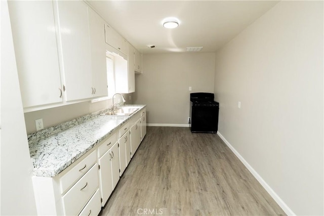 kitchen with visible vents, baseboards, a sink, white cabinetry, and light wood-type flooring