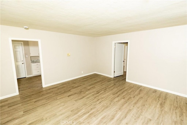 empty room with light wood-type flooring, baseboards, and a textured ceiling