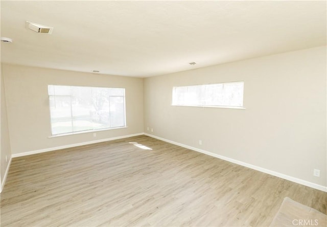 empty room with visible vents, light wood-type flooring, and baseboards