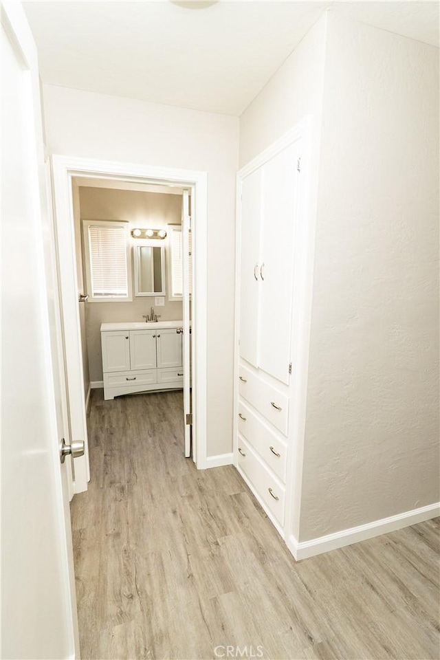 hallway with a sink, baseboards, and light wood-style floors