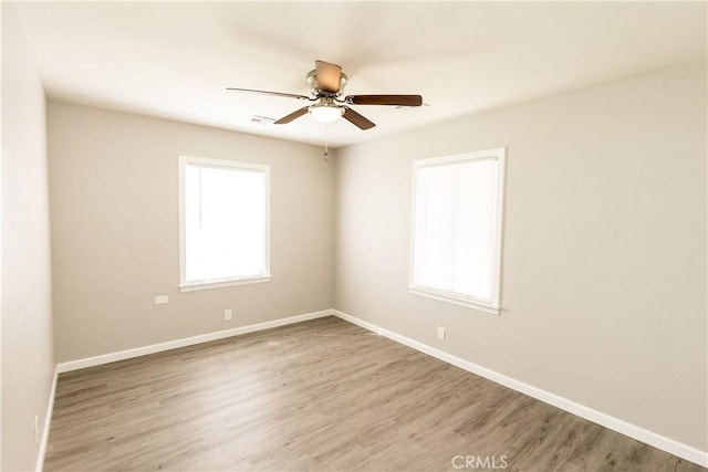 spare room with ceiling fan, visible vents, baseboards, and wood finished floors