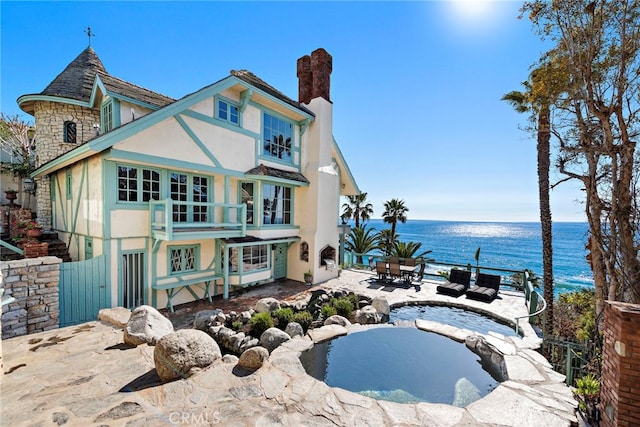 back of property featuring a water view, stucco siding, a chimney, a balcony, and a patio