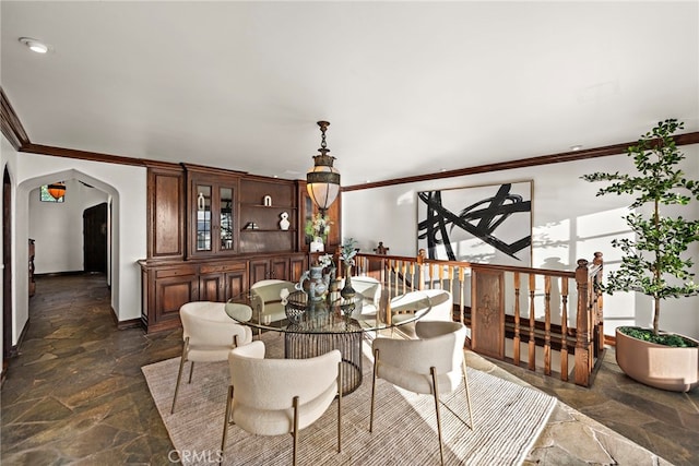 dining space featuring stone tile floors, crown molding, arched walkways, and baseboards