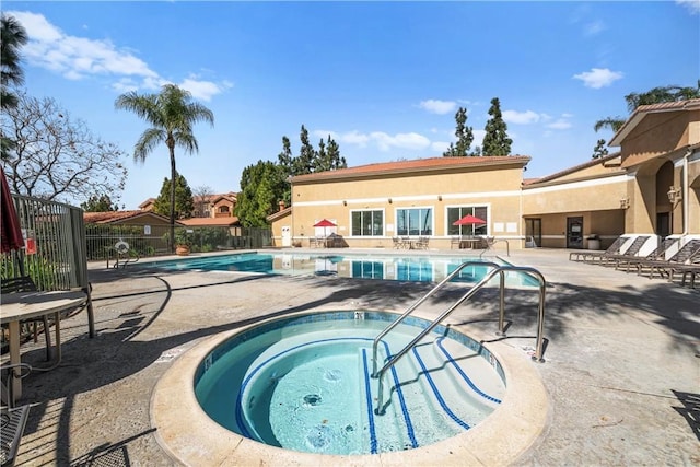 community pool with a patio, fence, and a hot tub