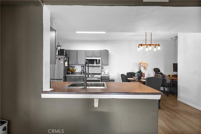 kitchen with wood finished floors, a peninsula, a sink, gray cabinetry, and appliances with stainless steel finishes