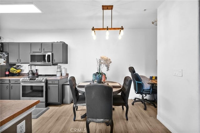 kitchen featuring baseboards, gray cabinetry, stainless steel appliances, light wood-style floors, and pendant lighting