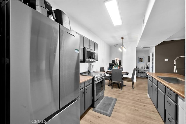 kitchen with gray cabinetry, light wood-type flooring, light countertops, stainless steel appliances, and a sink