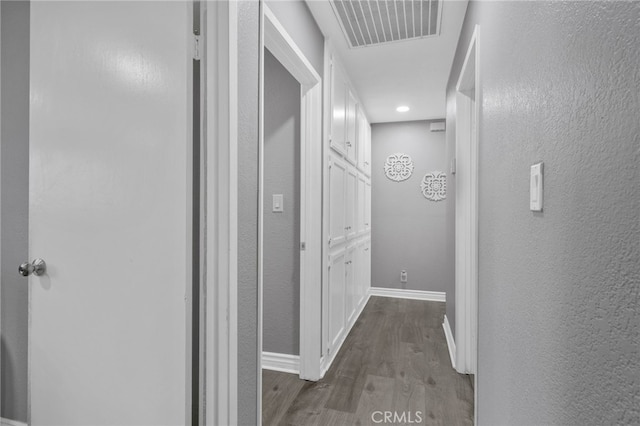 hall with a textured wall, baseboards, visible vents, and dark wood-style flooring