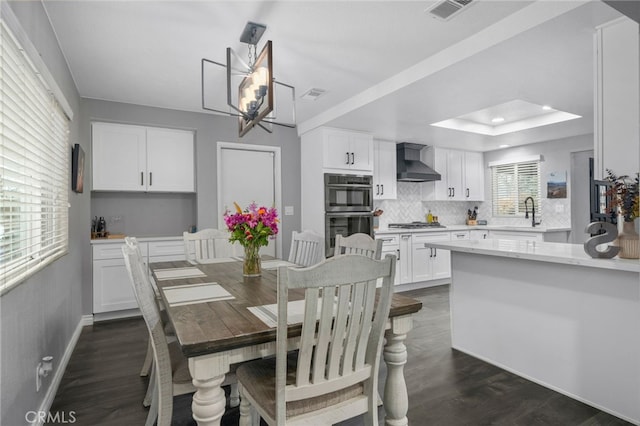 dining area with dark wood finished floors, visible vents, baseboards, and a tray ceiling