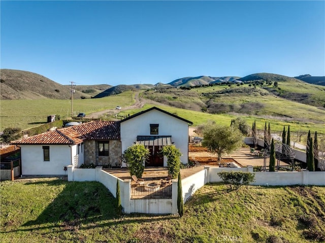 back of property with a tiled roof, a mountain view, stucco siding, and fence