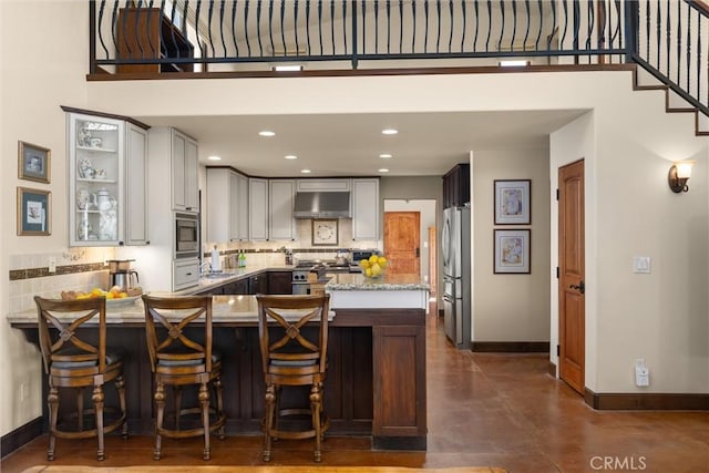 kitchen with under cabinet range hood, a sink, tasteful backsplash, stainless steel appliances, and a peninsula