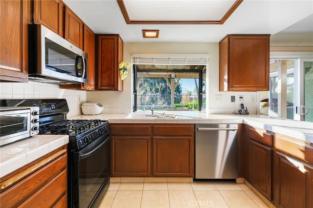 kitchen with backsplash, tile countertops, appliances with stainless steel finishes, brown cabinetry, and light tile patterned floors