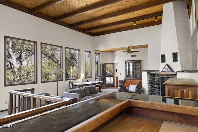 living area featuring beam ceiling, wood finished floors, a fireplace, wood ceiling, and a towering ceiling