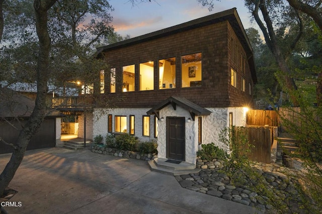 view of front facade featuring stone siding, concrete driveway, and fence