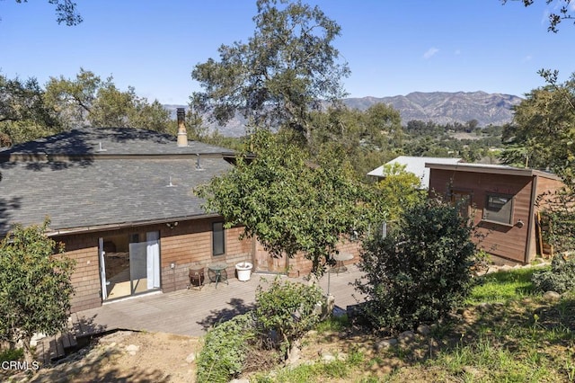 back of property with a deck with mountain view and a shingled roof