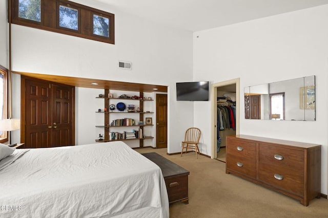 bedroom with visible vents, a high ceiling, a closet, a walk in closet, and light colored carpet