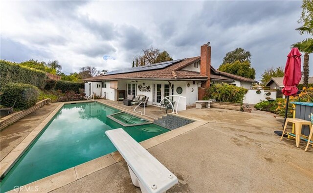 rear view of property with a fenced in pool, a chimney, french doors, a patio area, and roof mounted solar panels