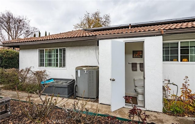 rear view of property with roof mounted solar panels, stucco siding, and cooling unit