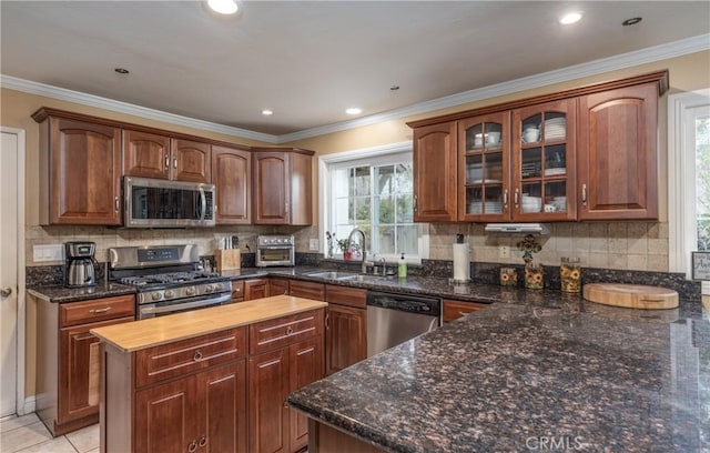 kitchen with a center island, ornamental molding, light tile patterned floors, stainless steel appliances, and a sink