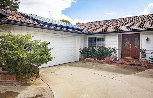 single story home with concrete driveway, a tiled roof, an attached garage, and roof mounted solar panels