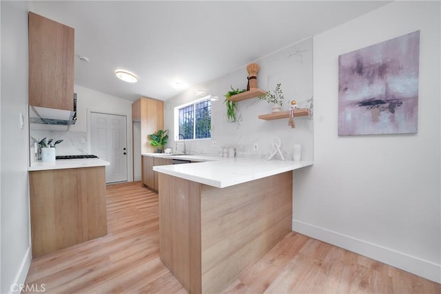 kitchen featuring a sink, light wood finished floors, a peninsula, and light countertops